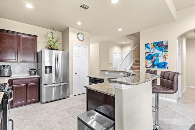 kitchen with light tile patterned floors, visible vents, a kitchen breakfast bar, arched walkways, and stainless steel appliances