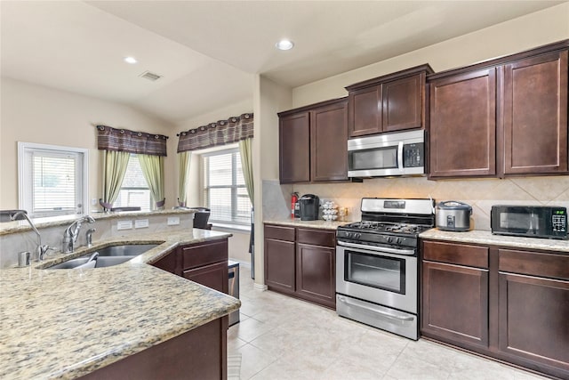 kitchen featuring lofted ceiling, light stone counters, a sink, decorative backsplash, and stainless steel appliances