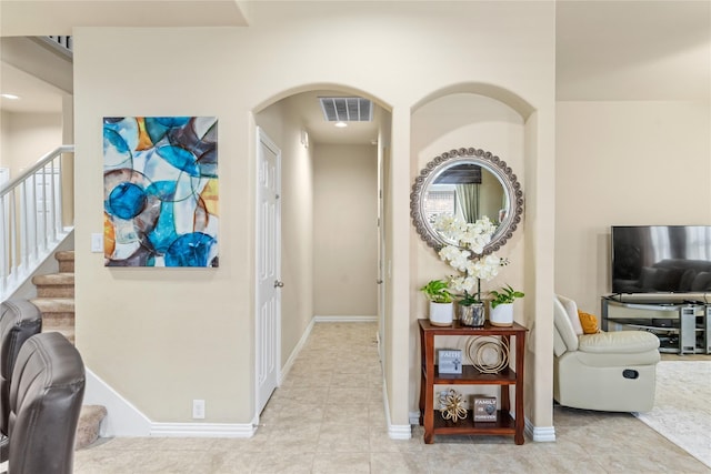 corridor featuring baseboards, visible vents, stairs, tile patterned flooring, and arched walkways