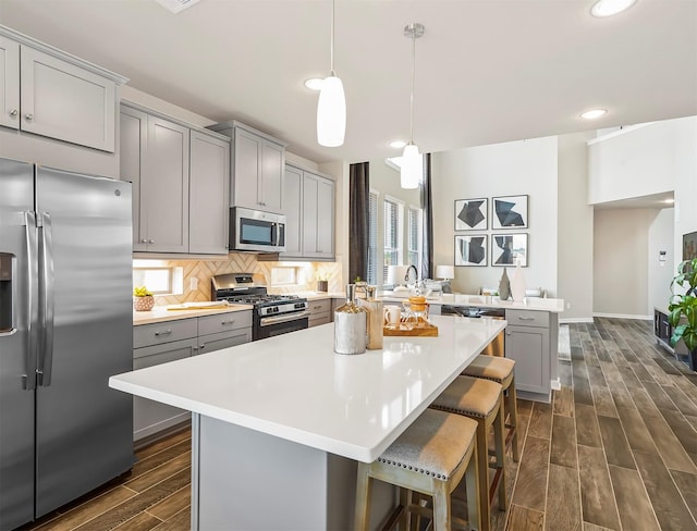 kitchen featuring gray cabinets, dark wood-type flooring, light countertops, appliances with stainless steel finishes, and a kitchen island