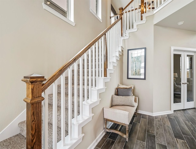 stairs featuring french doors, wood finished floors, baseboards, and a high ceiling
