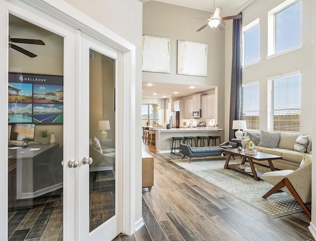 living room featuring ceiling fan, a towering ceiling, and wood finished floors