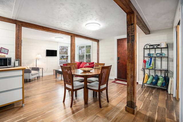 dining area featuring wooden walls, wood-type flooring, and a textured ceiling