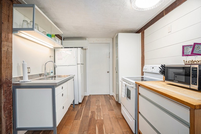 kitchen with butcher block countertops, white appliances, wood-type flooring, a sink, and open shelves