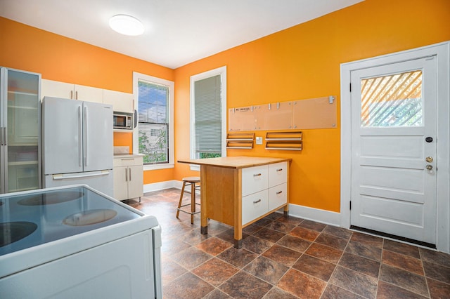 kitchen featuring baseboards, white appliances, white cabinetry, and plenty of natural light