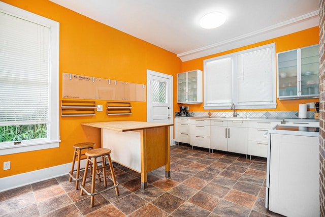 kitchen featuring white cabinetry, baseboards, glass insert cabinets, and stone tile flooring