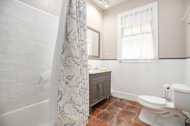 full bath with toilet, shower / bath combo with shower curtain, vanity, stone finish floor, and wainscoting