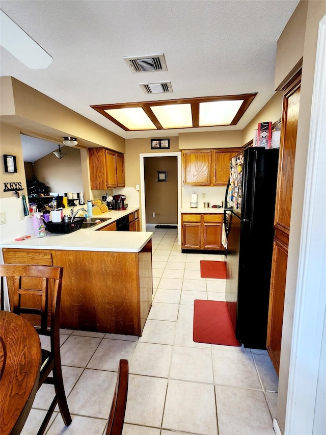 kitchen with brown cabinetry, visible vents, a peninsula, black appliances, and light countertops