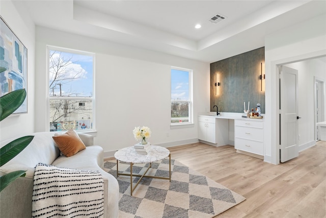 sitting room with a raised ceiling, a wealth of natural light, light wood-style flooring, and visible vents