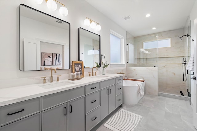 full bath with double vanity, a marble finish shower, a freestanding tub, and a sink
