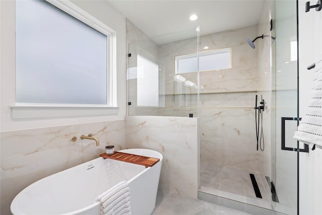 bathroom featuring tile walls, a marble finish shower, and a freestanding tub