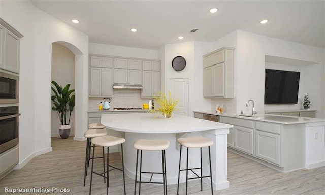 kitchen with light wood-style flooring, a sink, a kitchen breakfast bar, light countertops, and tasteful backsplash