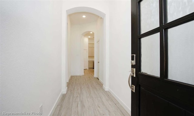 corridor with light wood-style flooring, baseboards, arched walkways, and recessed lighting