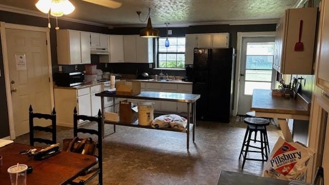 kitchen featuring freestanding refrigerator, under cabinet range hood, ornamental molding, white cabinets, and finished concrete flooring