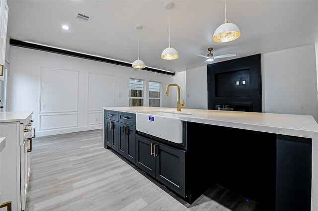 kitchen with a sink, light countertops, light wood finished floors, ceiling fan, and decorative light fixtures