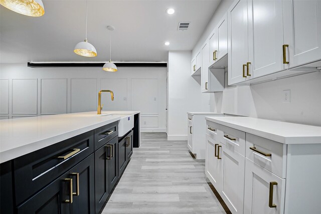 kitchen with a sink, light countertops, light wood finished floors, pendant lighting, and white cabinetry