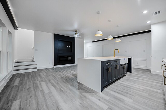kitchen featuring a sink, light countertops, light wood finished floors, a ceiling fan, and open floor plan