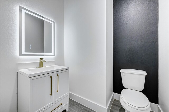 half bathroom with wood finished floors, vanity, and toilet