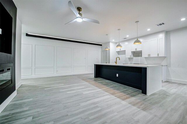 kitchen with a decorative wall, white cabinets, light wood-style floors, light countertops, and ceiling fan