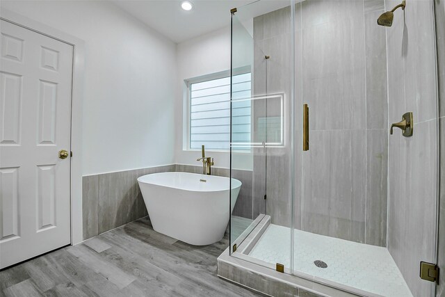 bathroom featuring a shower stall, a freestanding bath, a wainscoted wall, wood finished floors, and recessed lighting