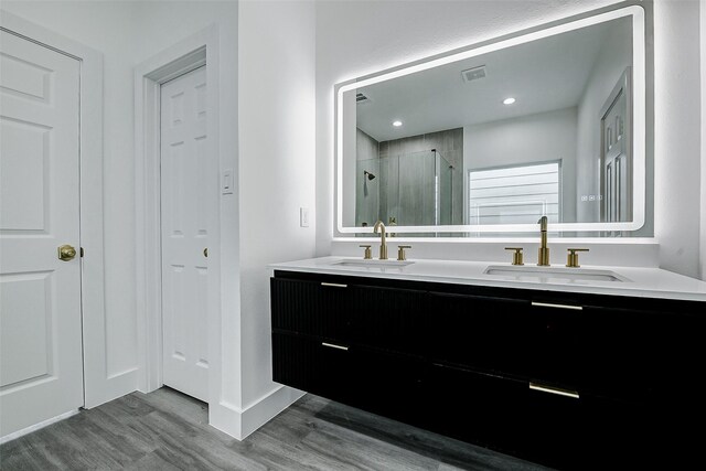 bathroom featuring a sink, double vanity, a stall shower, and wood finished floors