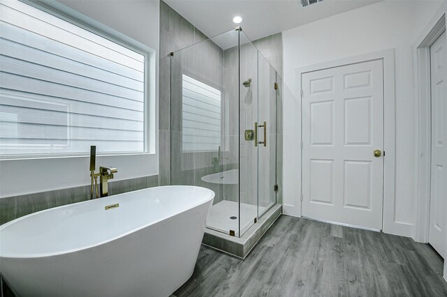 full bathroom with wood finished floors, a soaking tub, and a shower stall