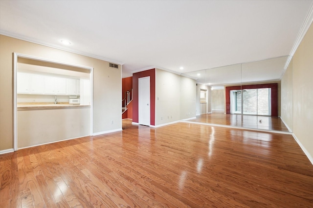 unfurnished living room featuring stairs, visible vents, crown molding, light wood-style flooring, and baseboards