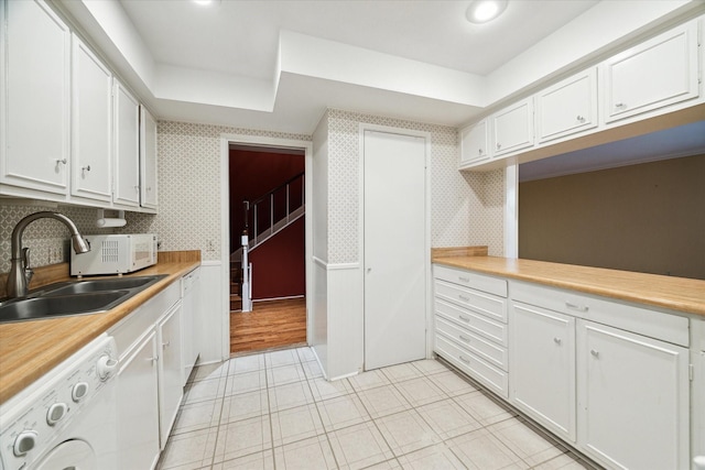 kitchen with washer / clothes dryer, a sink, white cabinetry, a raised ceiling, and light countertops