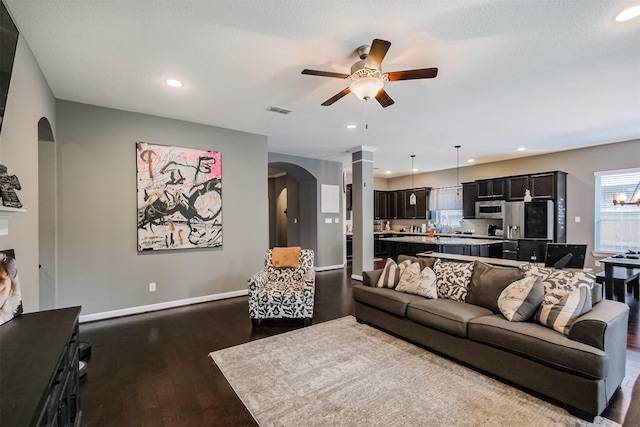 living room featuring a ceiling fan, baseboards, visible vents, dark wood-type flooring, and arched walkways