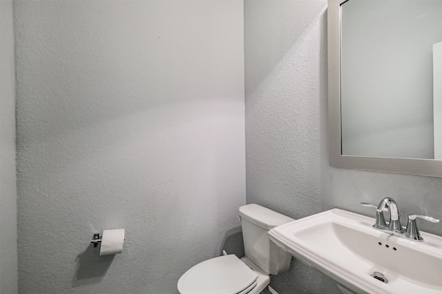 bathroom with toilet, a sink, and a textured wall