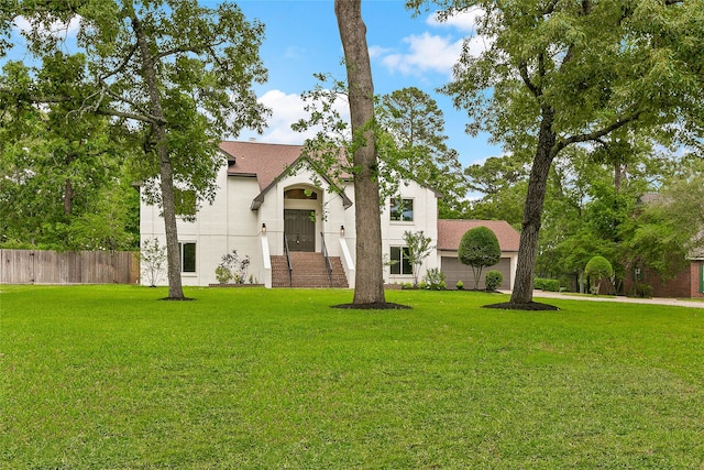 view of front facade with a garage, stucco siding, fence, a front lawn, and roof with shingles