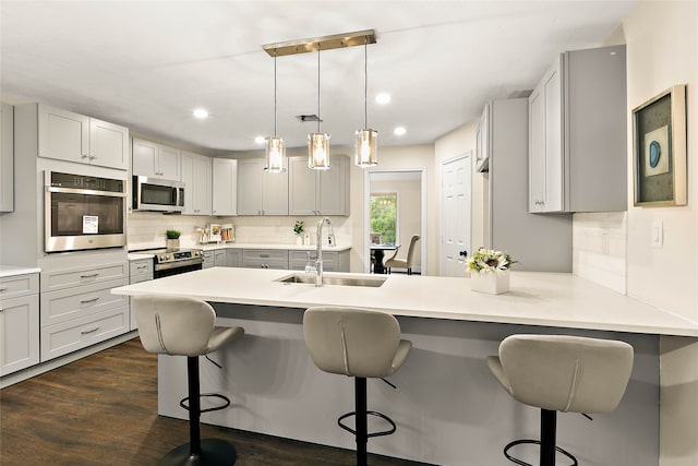 kitchen featuring a sink, a peninsula, stainless steel appliances, a kitchen breakfast bar, and decorative backsplash