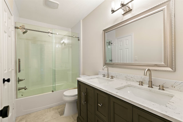 full bath featuring toilet, double vanity, a sink, and shower / bath combination with glass door
