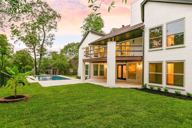 rear view of house featuring a patio, a lawn, a fenced in pool, and a balcony