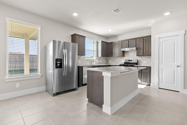 15214 Prairie Mill Dr, New Caney, TX 77357 - kitchen with appliances with stainless steel finishes, dark brown cabinetry, backsplash, under cabinet range hood, and a center island