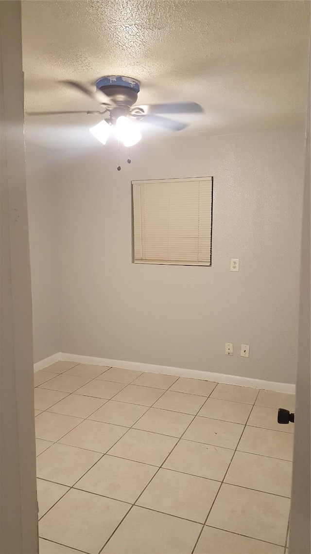 spare room with a ceiling fan, baseboards, light tile patterned floors, and a textured ceiling