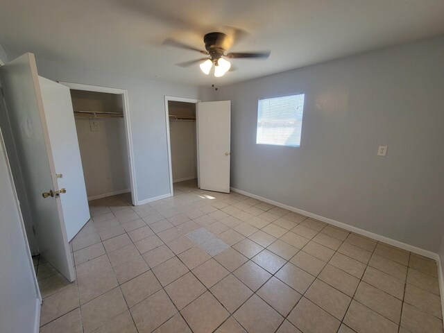 unfurnished bedroom with light tile patterned floors, baseboards, multiple closets, and ceiling fan