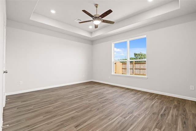 spare room featuring wood finished floors, a ceiling fan, a tray ceiling, baseboards, and recessed lighting