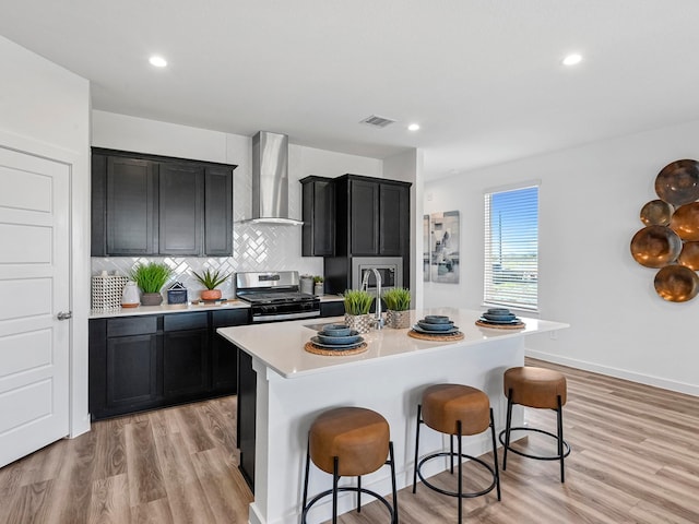 kitchen featuring light countertops, stainless steel gas range, visible vents, wall chimney range hood, and dark cabinetry