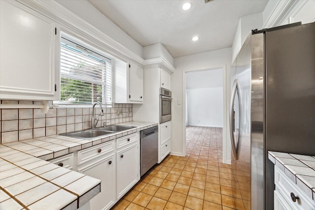 kitchen with appliances with stainless steel finishes, tile counters, a sink, white cabinetry, and decorative backsplash
