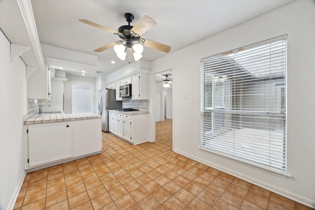 kitchen featuring tile countertops, ceiling fan, white cabinetry, decorative backsplash, and appliances with stainless steel finishes