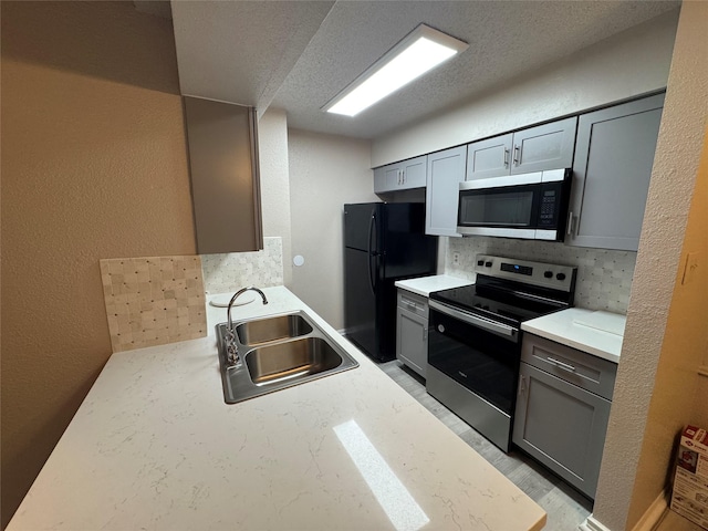 kitchen featuring a textured ceiling, a sink, light countertops, appliances with stainless steel finishes, and a textured wall