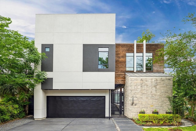 contemporary home featuring an attached garage, stone siding, concrete driveway, metal roof, and a standing seam roof