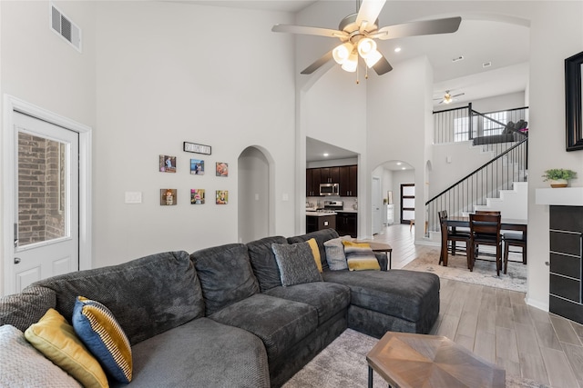 1226 Tilia Creek Ln, Montgomery, TX 77316 - living room featuring arched walkways, a ceiling fan, light wood-style flooring, stairs, and a high ceiling