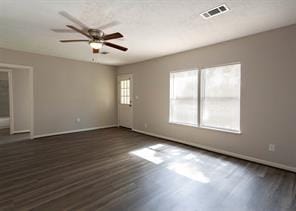 empty room with baseboards, visible vents, a ceiling fan, and dark wood-type flooring