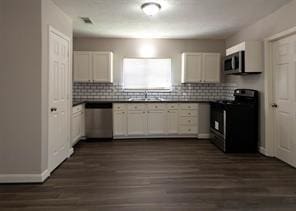 kitchen with a sink, stainless steel appliances, white cabinetry, decorative backsplash, and dark countertops