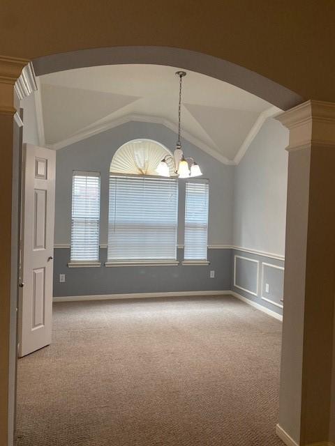 empty room with vaulted ceiling, carpet floors, arched walkways, plenty of natural light, and a notable chandelier