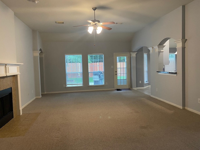 unfurnished living room with a tile fireplace, decorative columns, carpet floors, ceiling fan, and arched walkways