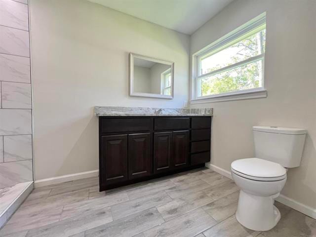 bathroom featuring toilet, vanity, wood tiled floor, baseboards, and tiled shower