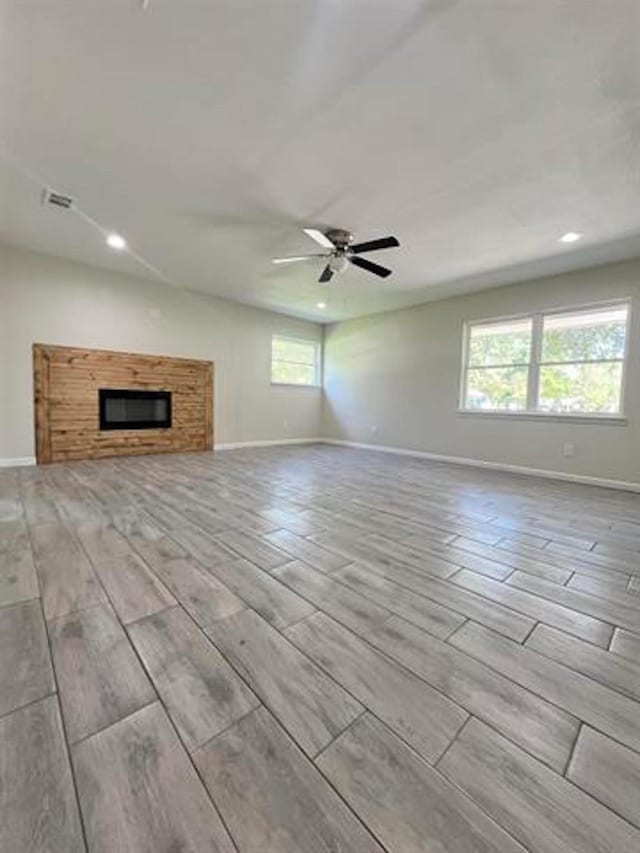 unfurnished living room with ceiling fan, baseboards, wood finish floors, and a glass covered fireplace